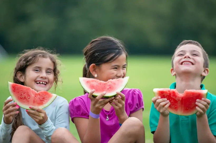 Three children eating watermelon and smiling.