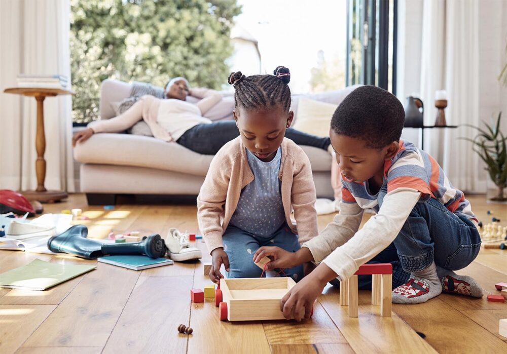 Girl and boy play while mum is on the couch.