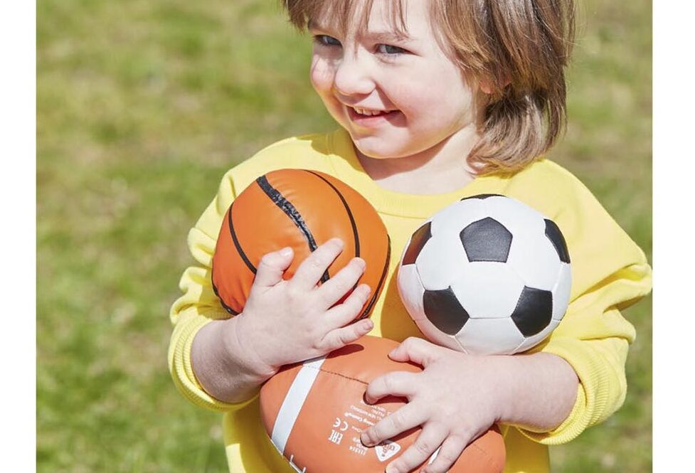 child holding different balls for games.