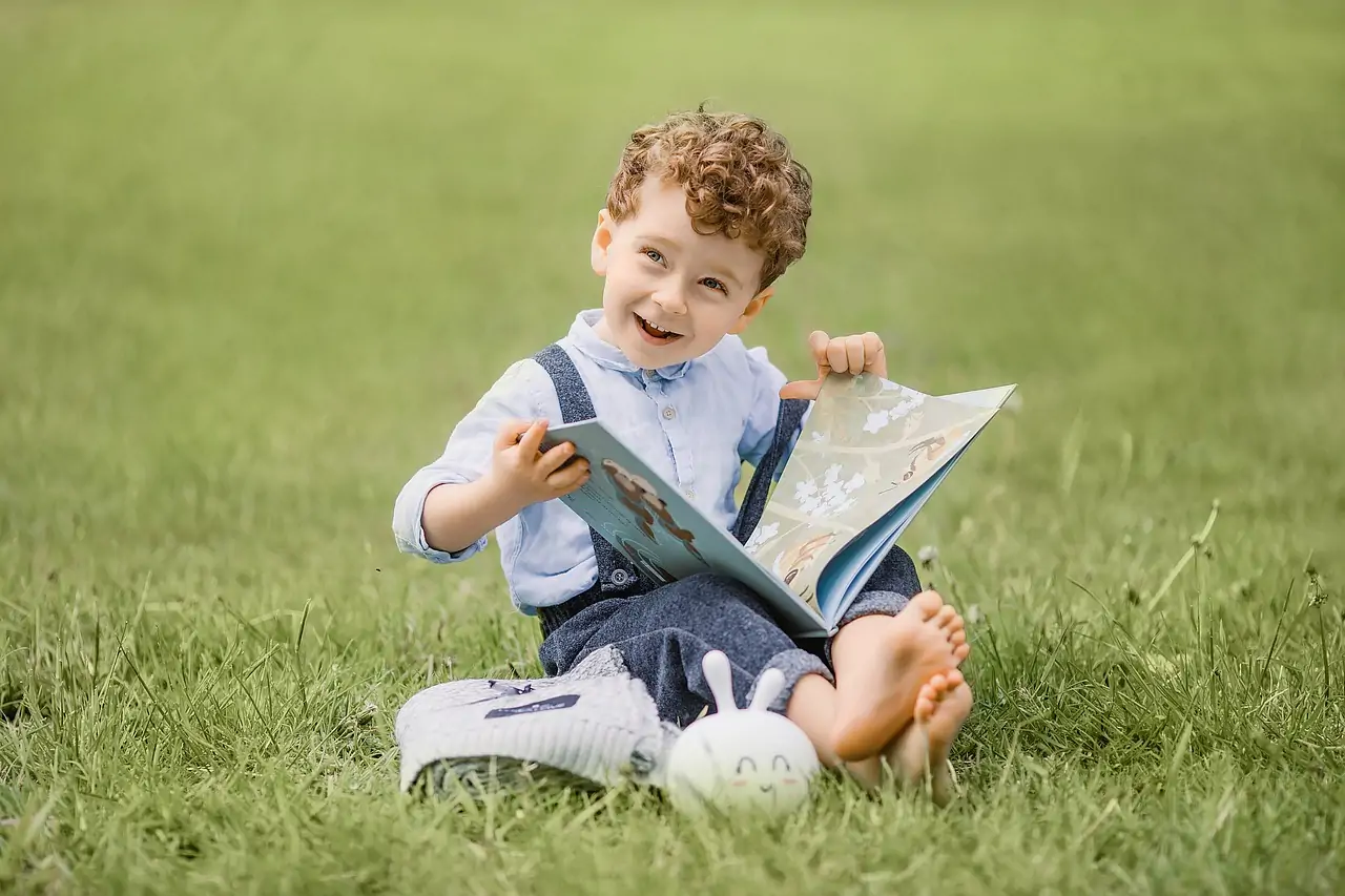 boy reading book in field.