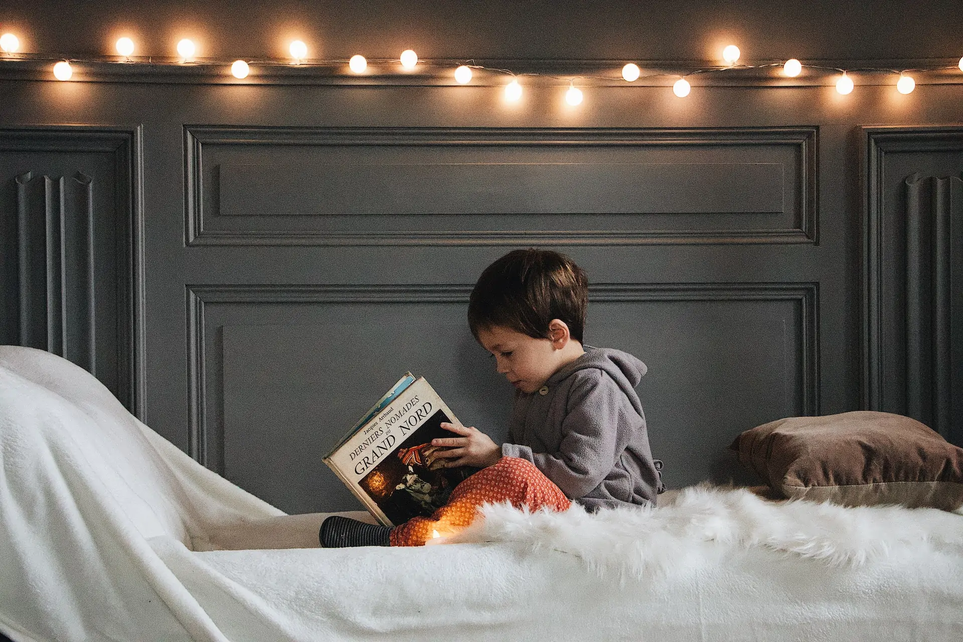 Boy sits on bed reading his book.