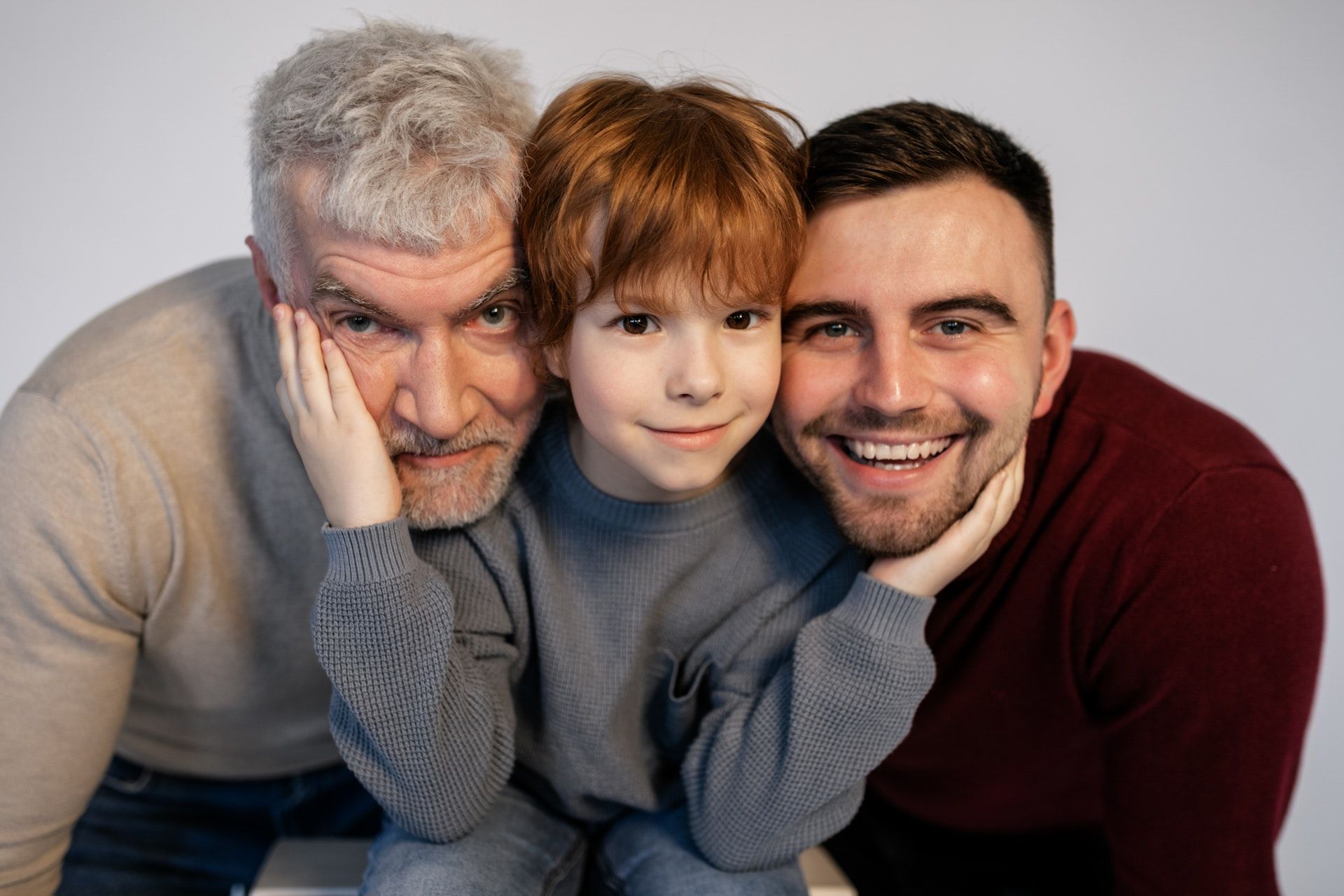 A boy in-between his father and grandfather holds their face for a photo.