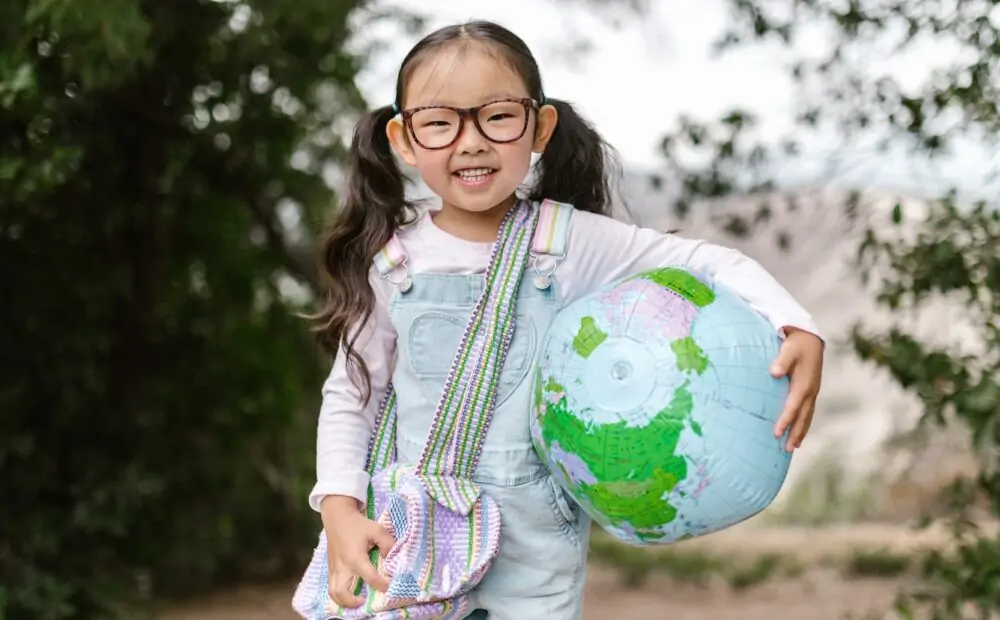 Child holds a globe and a bag in the outdoors.