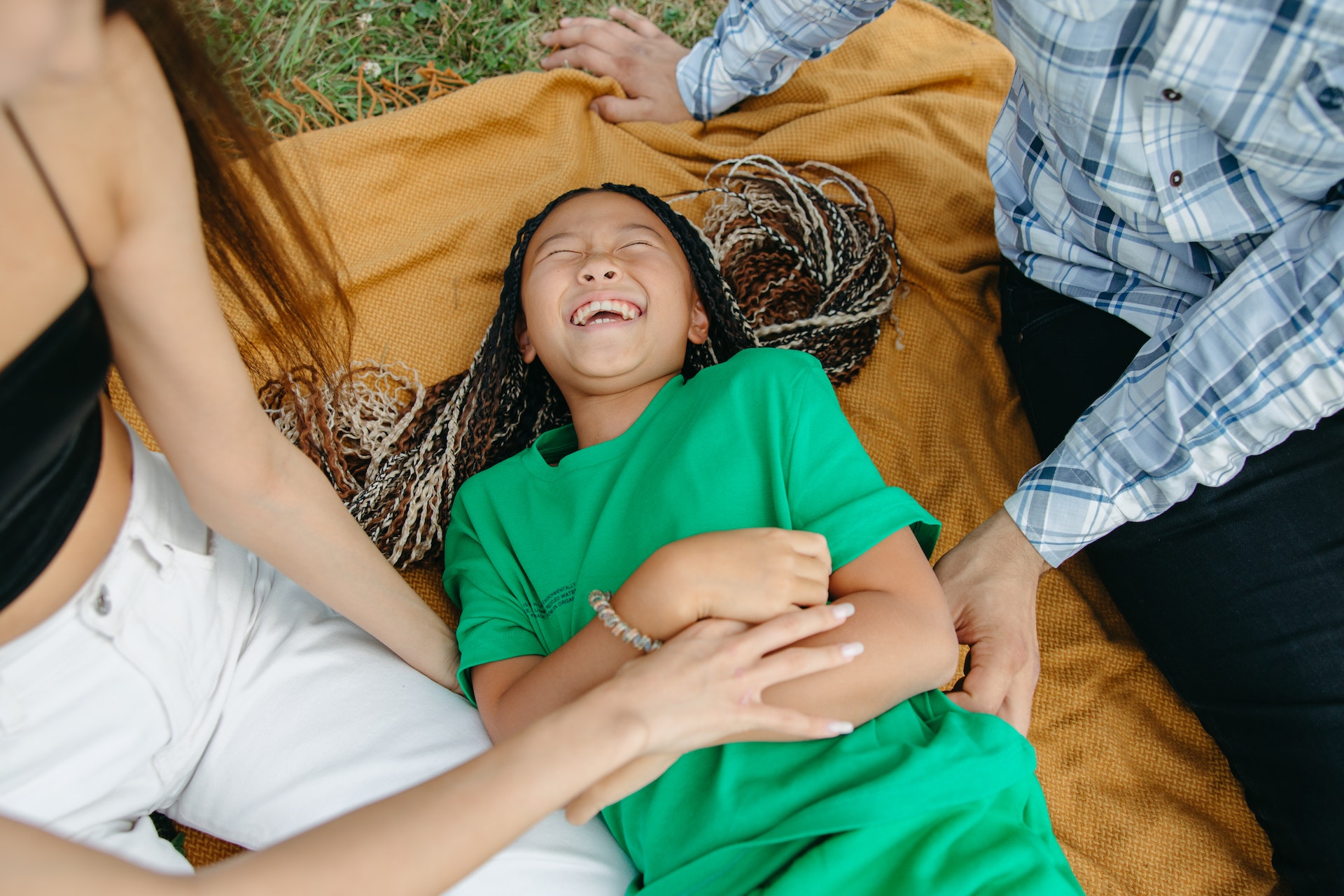 Child laughs while on a picnic matt next to her parents.