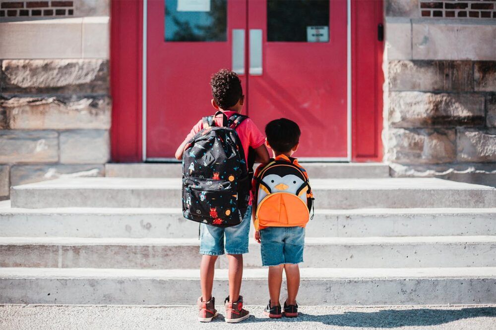 two boys standing in front of the school steps with backpacks on