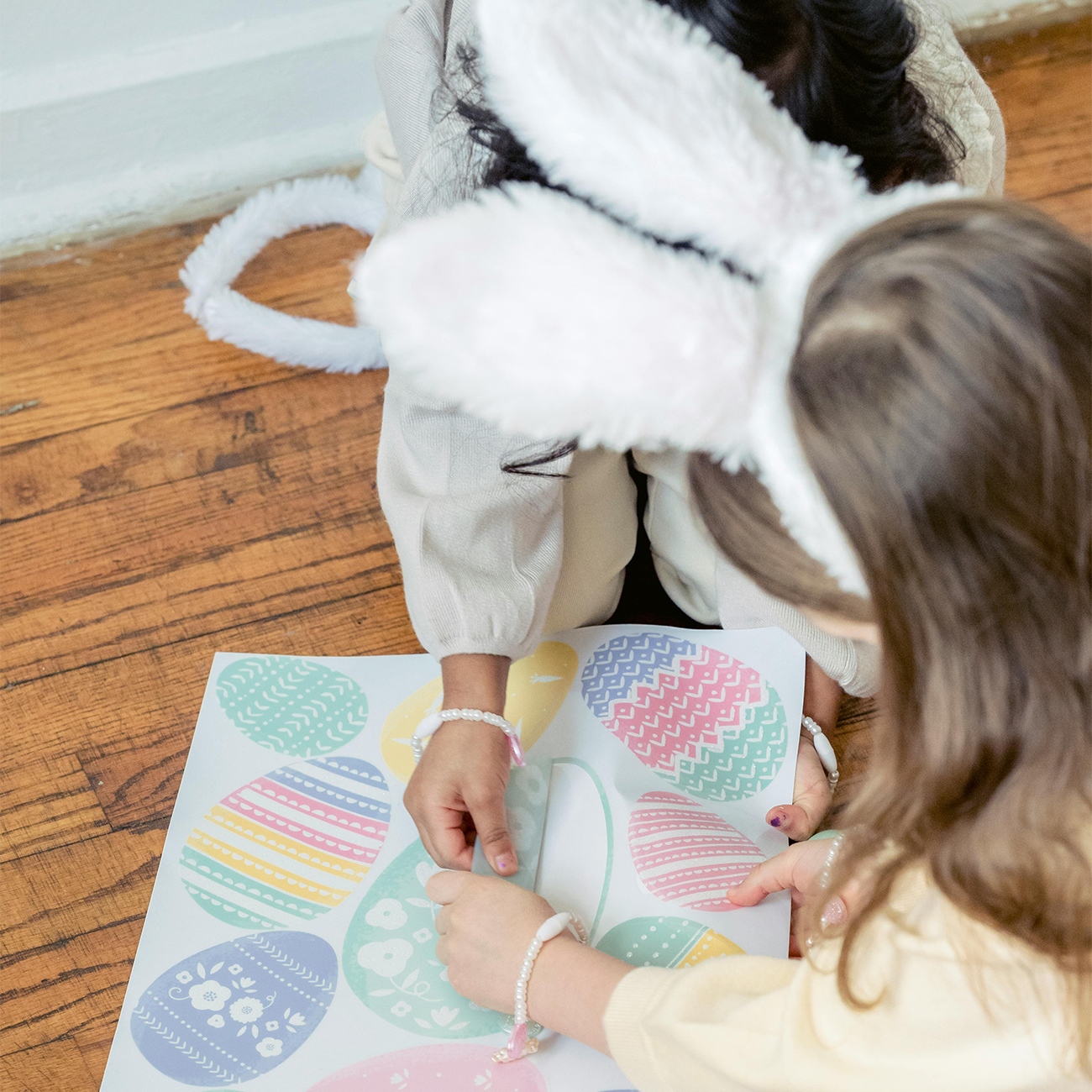 two children with bunny ears on, sitting making easter egg decorations