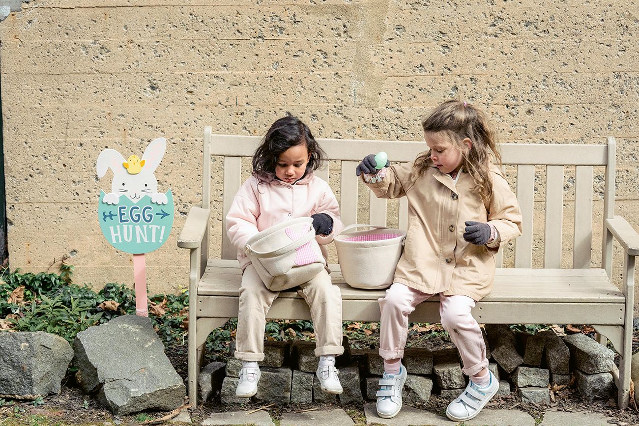 two children sitting on a bench with an easter basket full of eggs