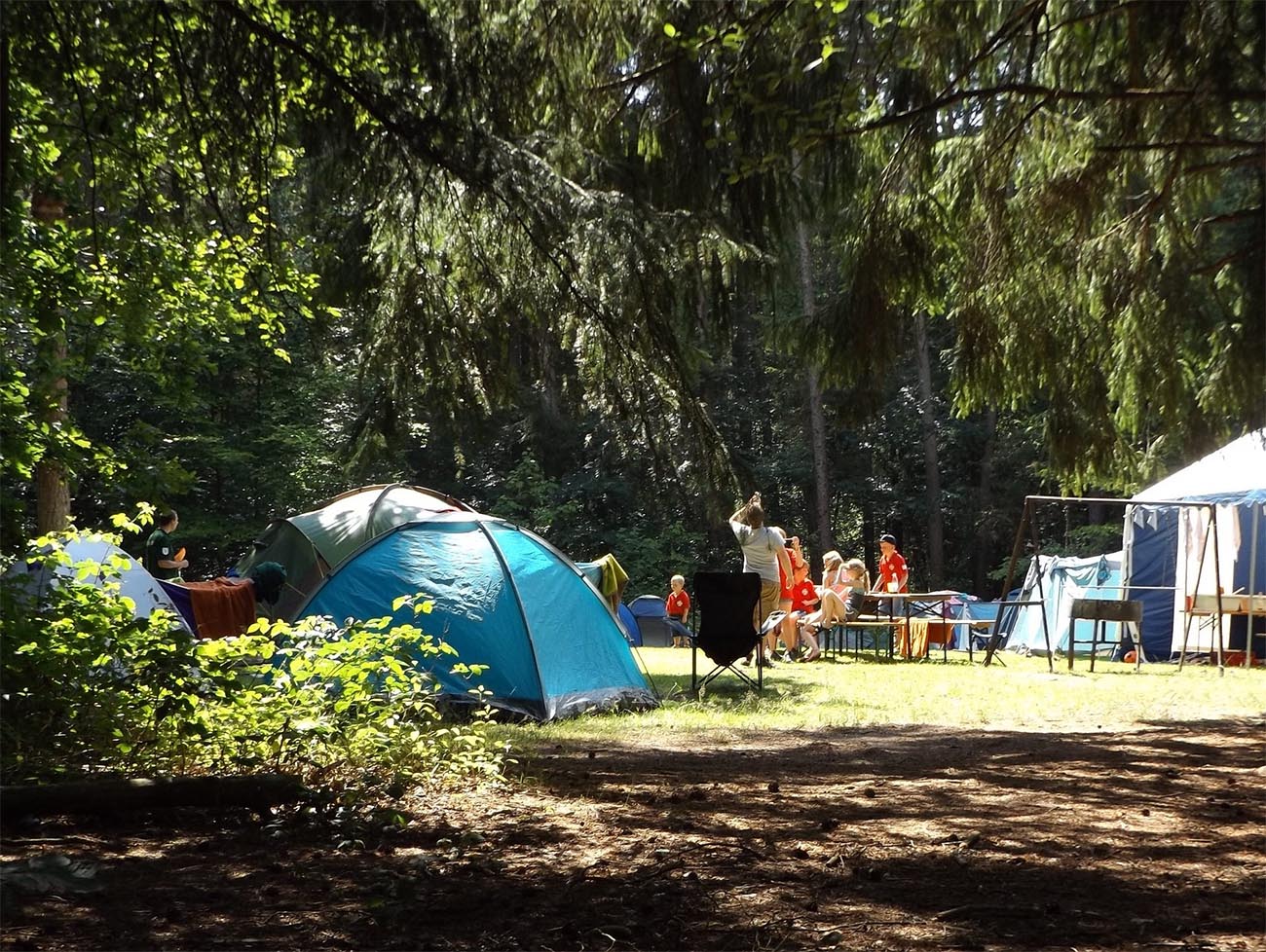 in the distance is a group of tents and a family, deep in the woods