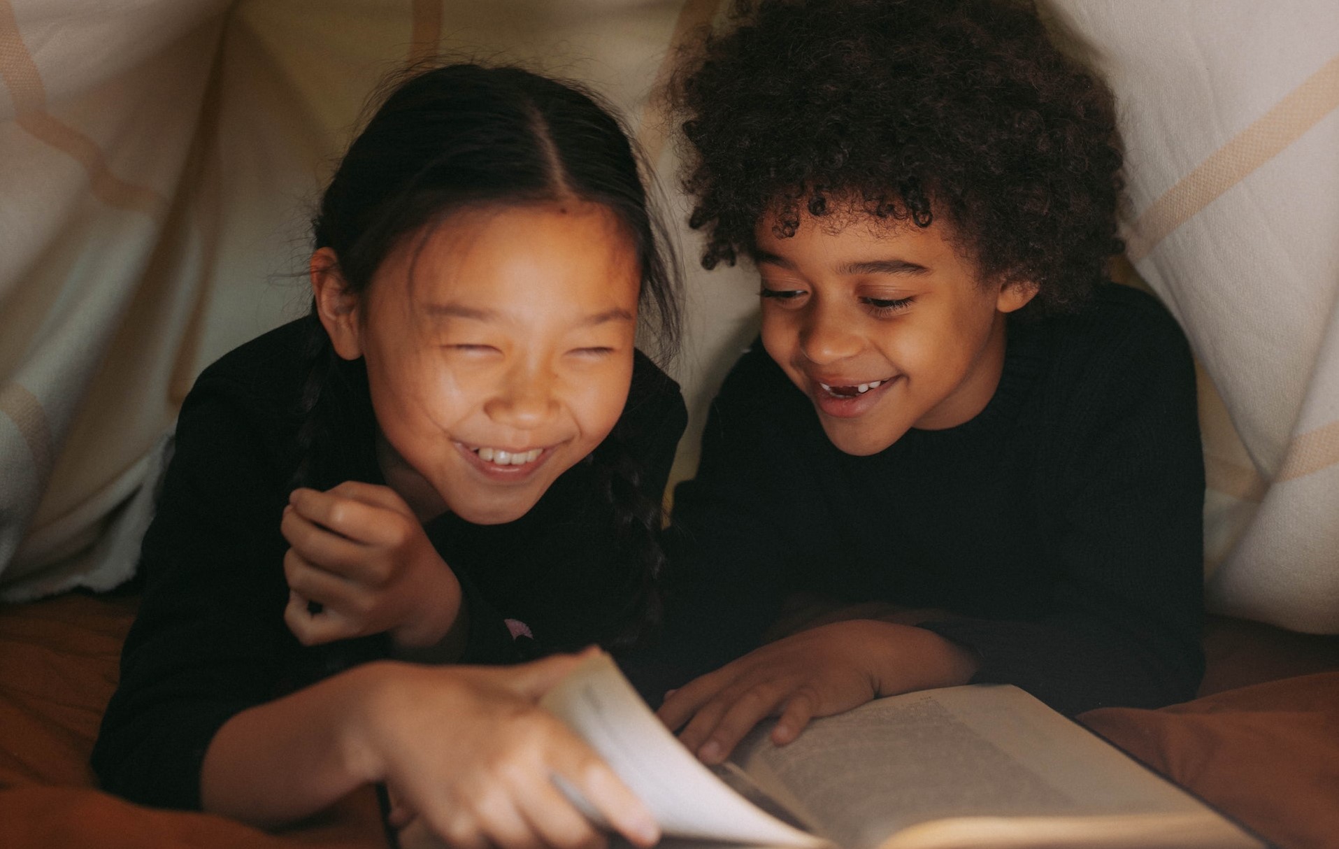 Kids reading under a blanket before bed.