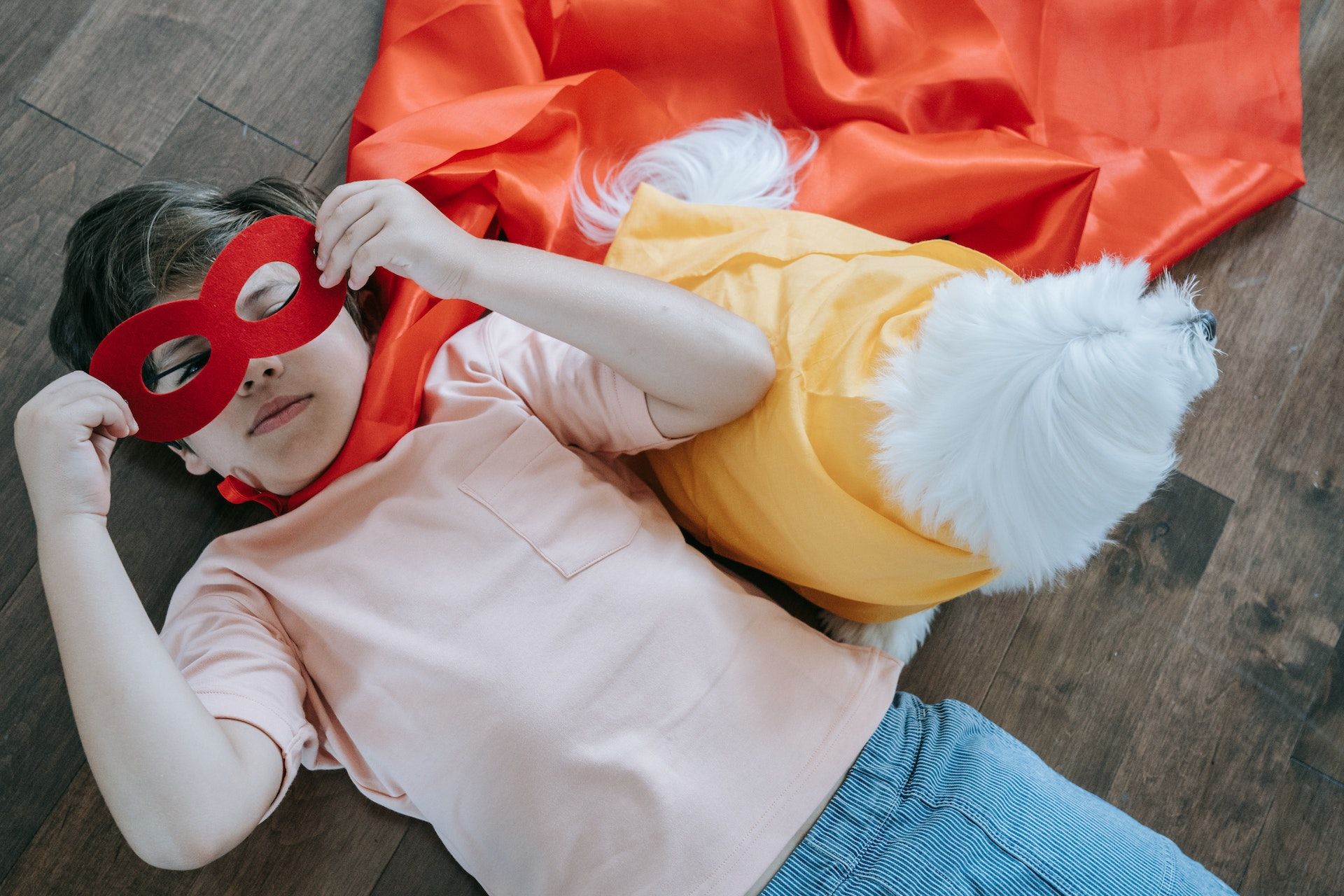 Boy wearing mask and cape while laying on floor.
